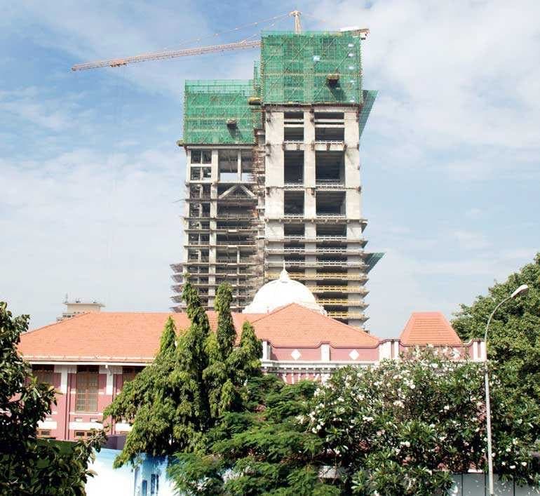 Tower under construction with a crane rising above a heritage building in an urban setting